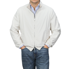 Man in a beige nougat nylon reversible Fedeli blouson jacket over a blue striped shirt with jeans, against a gray background.