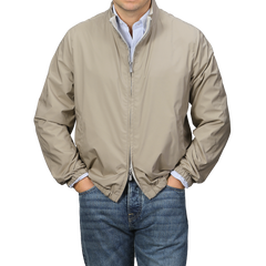 A person wearing a Fedeli Beige Nougat Nylon Reversible Blouson Jacket with a two-way zip closure, paired with blue jeans, stands with hands in pockets against a neutral background.