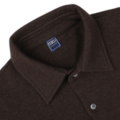 A close-up of a dark brown felted cashmere overshirt with a collar and buttons, featuring a label that reads "Fedeli, Made in Italy." This luxurious garment offers both style and comfort with its regular fit design.