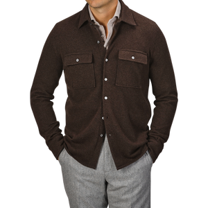 A man wearing a Fedeli Dark Brown Felted Cashmere Overshirt with front pockets and gray trousers, hands casually tucked in his pockets.