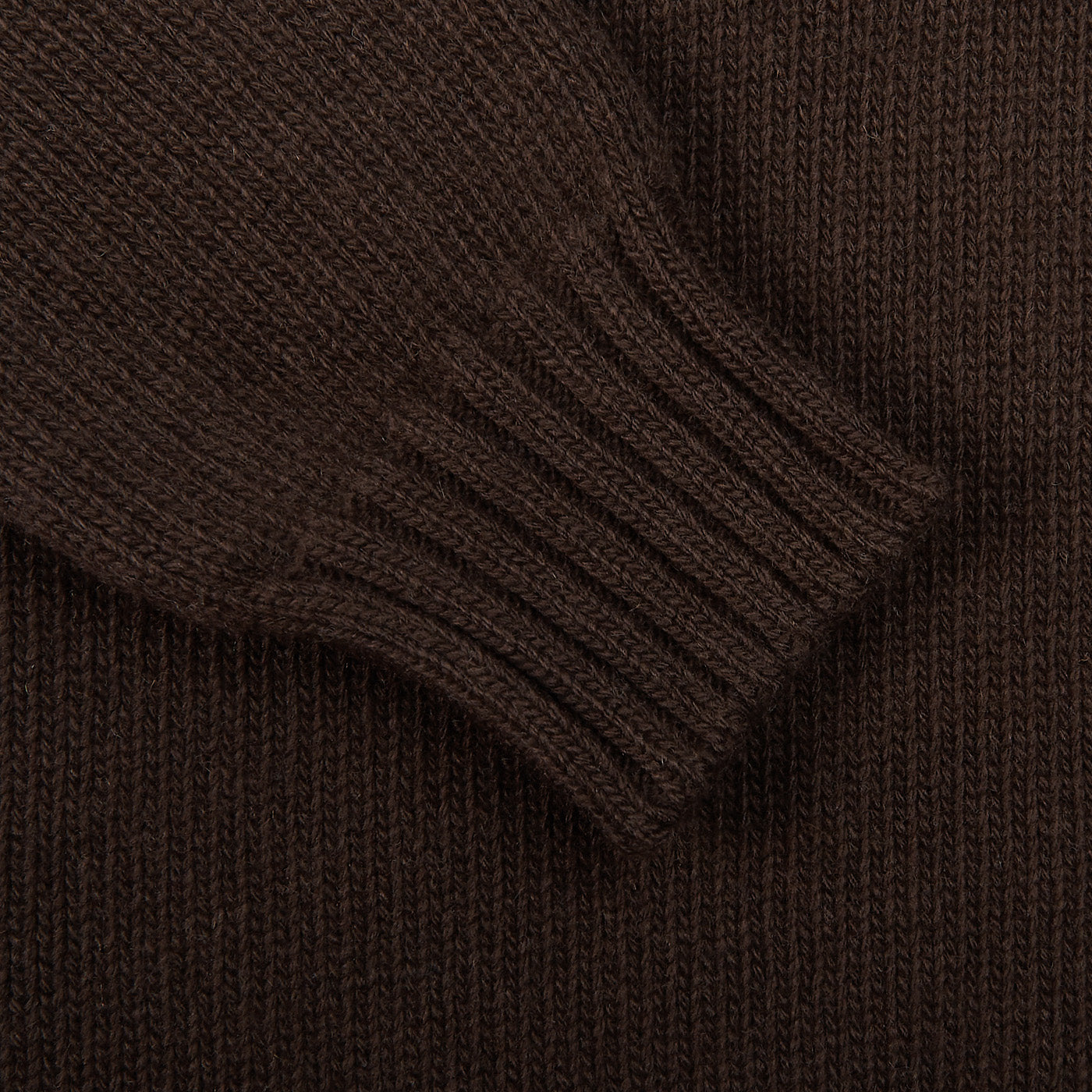 A detailed view of the sleeve from Fedeli's Dark Brown Wool Cashmere Rollneck, featuring a ribbed cuff, is set against a matching knitted fabric backdrop, highlighting the exquisite craftsmanship.