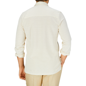 Rear view of a person wearing a Fedeli Ecru Cotton Linen Piquet Polo Shirt and beige trousers against a blue background.