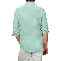 A person wearing a Fedeli slim fit Green White Striped Cotton Beach Shirt with rolled-up sleeves and white pants faces away from the camera.