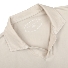 Close-up of the Light Beige Organic Cotton Capri Collar Polo Shirt by Fedeli shows an open capri collar and a visible inner label reading, "Everything with a past is working for future." Crafted from organic Giza cotton, it blends luxury casual-wear with sustainability.