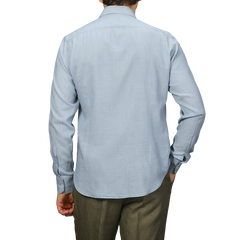 A person wears a Fedeli light blue cotton denim shirt and gray pants, seen from the back against a plain background.