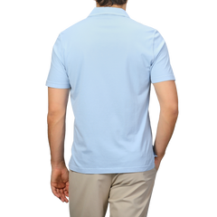 A person is seen from the back in a luxurious Fedeli light blue Capri collar polo shirt, crafted from organic cotton, paired with beige pants against a plain backdrop.