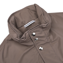 Close-up of a brown field jacket collar with metal buttons and a striped fabric tab inside. This Light Brown Nylon Rainproof Field Jacket, designed by Fedeli in a slim fit, is both wind and water-resistant.