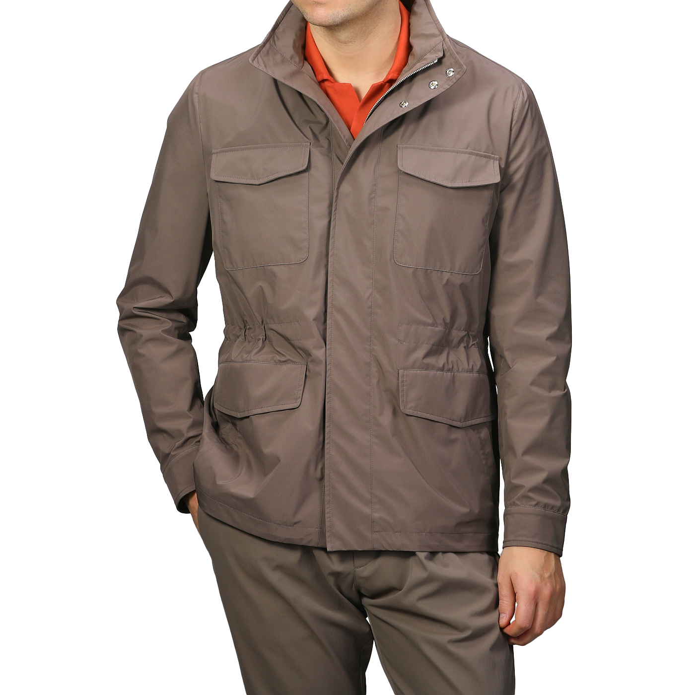 A person is wearing a Light Brown Nylon Rainproof Field Jacket by Fedeli, featuring multiple pockets and a slim fit, paired with matching pants. Beneath the wind and water-resistant jacket is an orange shirt, adding a pop of color to their outfit.