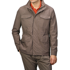 A person is wearing a Light Brown Nylon Rainproof Field Jacket by Fedeli, featuring multiple pockets and a slim fit, paired with matching pants. Beneath the wind and water-resistant jacket is an orange shirt, adding a pop of color to their outfit.