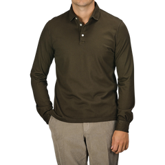 A person wearing a Fedeli Moss Green Organic Cotton LS Polo Shirt and beige pants, standing with one hand in their pocket against a plain background, exudes luxury casual-wear.