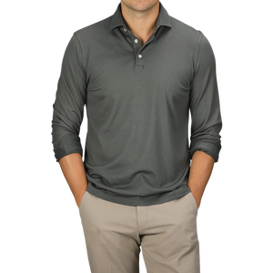 A man wearing a Muted Green Organic Cotton LS Polo Shirt by Fedeli and beige pants stands with his hands in his pockets against a plain background, embodying luxury casual-wear.