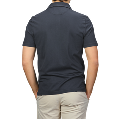 A person in a Navy Blue Organic Cotton Polo Shirt by Fedeli and light pants is shown from the back, standing against a neutral background.