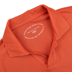 A close-up of the Fedeli Orange Organic Cotton Capri Collar Polo Shirt showcases its luxury casual-wear essence, with a printed circular label inside the collar.