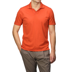 Elegantly attired in a Fedeli Orange Organic Cotton Capri Collar Polo Shirt and brown pants, a person stands out against a neutral backdrop.