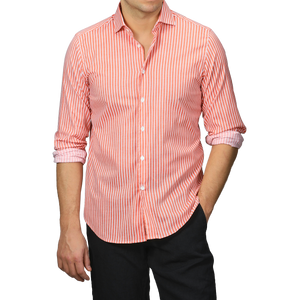 Dressed in a slim fit Orange White Striped Cotton Beach Shirt by Fedeli, a person with rolled-up sleeves stands stylishly against a plain background, paired elegantly with black pants.