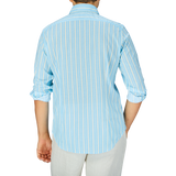 A person standing with their back to the camera, wearing a Fedeli Sky Blue Yellow Striped Cotton Beach Shirt and white pants.