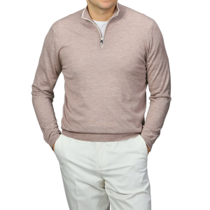 A person in a Fedeli Taupe Beige Cashmere Silk 1/4 Zip Sweater over a white shirt with white pants stands hands-in-pockets against a gray background.