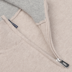 Close-up of the Fedeli Taupe Beige Wool Cashmere 1/4 Zip Sweater, showcasing its light beige knitted zip-up design. The image highlights a partially unzipped section with a silver zipper and a small brand tag attached to the zipper pull, exemplifying it as an ideal layering piece.