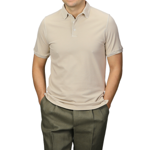 A man wearing a Washed Beige Cotton Pique Polo Shirt by Fedeli and olive pants stands with his hands in his pockets against a gray background.