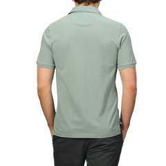 A person wearing a high-quality Fedeli Washed Light Green Cotton Pique Polo Shirt and dark pants is shown from the back against a gray background, ideal for summer attire.