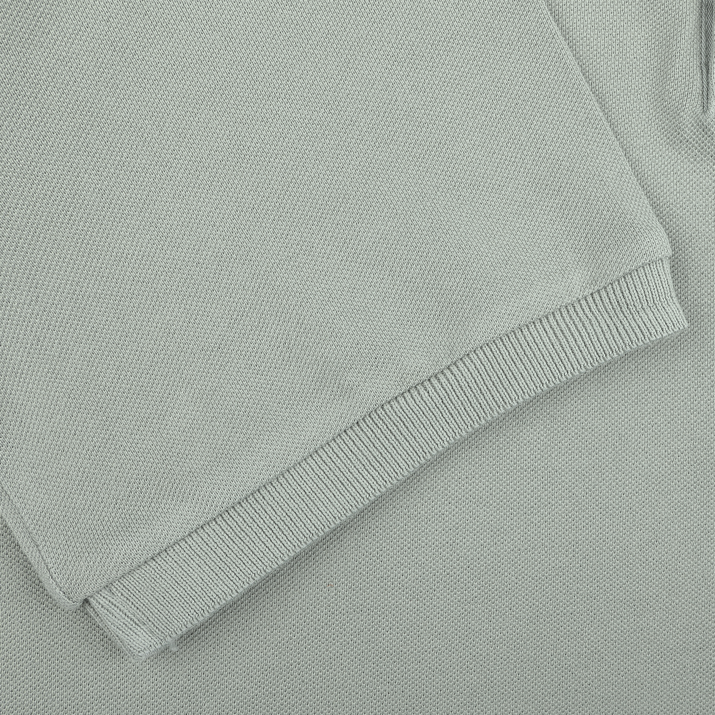 Close-up of a folded washed light green cotton pique polo shirt by Fedeli on a matching fabric surface, highlighting its texture and ribbed hem as a testament to superior quality.