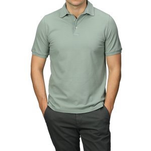 A person dressed in a Washed Light Green Cotton Pique Polo Shirt by Fedeli and dark pants, hands in pockets, ideal for a summer wardrobe.