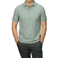 A person dressed in a Washed Light Green Cotton Pique Polo Shirt by Fedeli and dark pants, hands in pockets, ideal for a summer wardrobe.