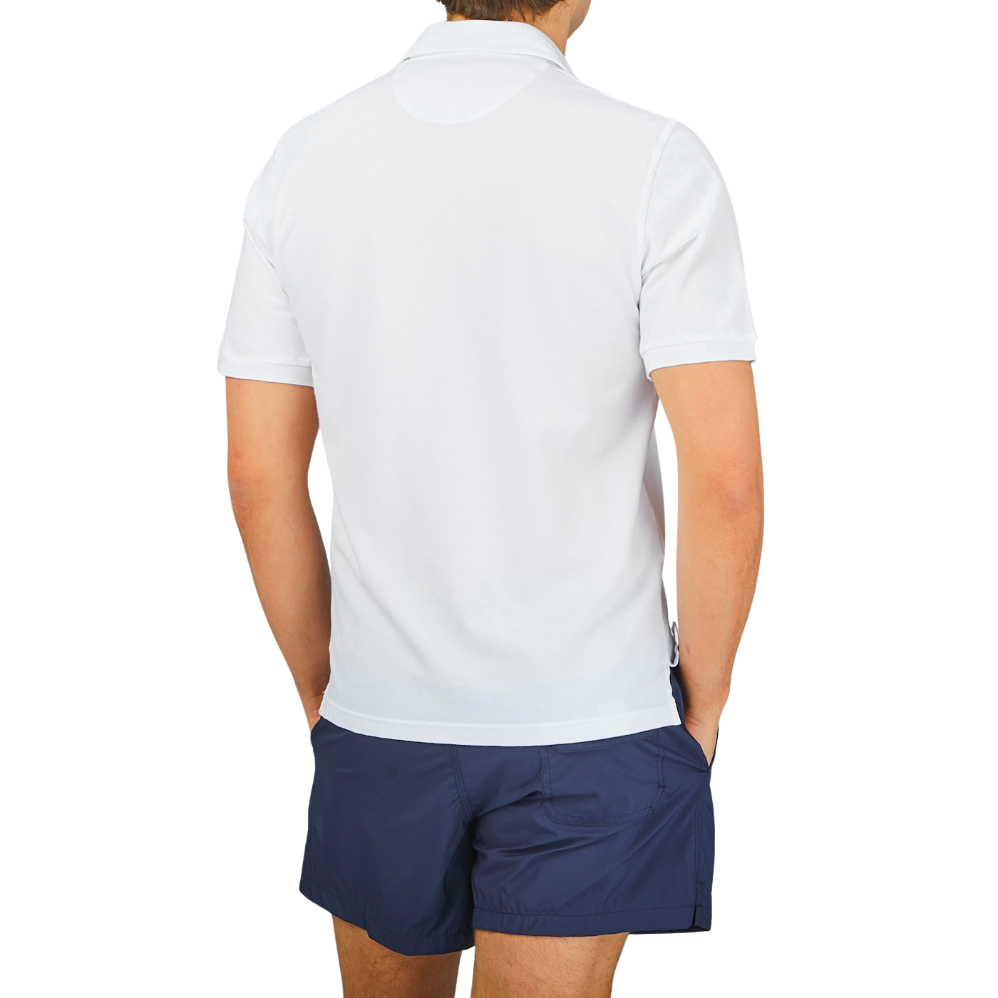The back view of a man wearing a Fedeli washed white cotton pique polo shirt with a washed finish and blue shorts.