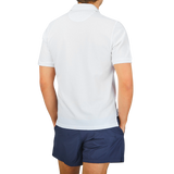 The back view of a man wearing a Fedeli washed white cotton pique polo shirt with a washed finish and blue shorts.