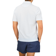 The back view of a man wearing a Fedeli washed white cotton pique polo shirt with a washed finish and blue shorts.