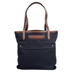 The Navy Blue Cotton Canvas Leather Tote Bag by Felisi boasts a design featuring vacchetta calf leather handles and accents. It includes a convenient front pocket with two snaps and a leather patch with an embossed motif.