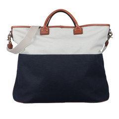 The Navy Grey Cotton Canvas Leather Travel Tote by Felisi showcases a stylish two-toned design with a white upper section and navy lower section, crafted from durable cotton canvas. It is equipped with brown vacchetta calf leather handles and a detachable beige shoulder strap, making it an ideal option for fashionable travel.