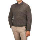 A person wearing a Filippo de Laurentiis Brown Melange Yak Cashmere Sweater—a seasonal staple—over a blue shirt and beige pants stands against a neutral background with hands in pockets.