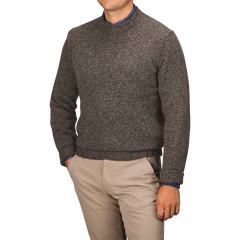 A person wearing a Filippo de Laurentiis Brown Melange Yak Cashmere Sweater—a seasonal staple—over a blue shirt and beige pants stands against a neutral background with hands in pockets.