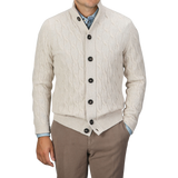 A person is wearing a Filippo de Laurentiis Cream Wool Cashmere Cableknit Button Cardigan over a blue shirt, paired with brown pants, standing against a plain background.