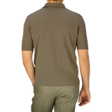 Rear view of a man in a Mole Grey Crepe Cotton Polo Shirt by Filippo de Laurentiis and green trousers standing against a light blue background.