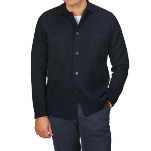 A person wearing a sophisticated button-up black shirt, inspired by timeless Italian fashion, featuring two chest pockets, and paired with dark pants from Filippo De Laurentiis stands with one hand in their pocket.