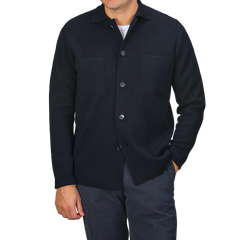 A person wearing a sophisticated button-up black shirt, inspired by timeless Italian fashion, featuring two chest pockets, and paired with dark pants from Filippo De Laurentiis stands with one hand in their pocket.