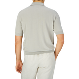 Man standing with his back to the camera wearing a slim fit Nebbia Grey Crepe Cotton Polo Shirt by Filippo de Laurentiis and white pants.