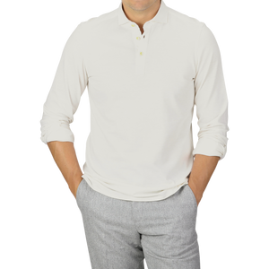 Man wearing a handmade Ecru Cotton Cashmere Jersey Polo Shirt by Finamore and gray slim-fit pants with hands in pockets, standing against a plain background.