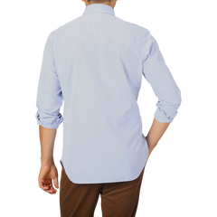 A person wearing a Finamore Light Blue Washed Cotton BD Shirt with the sleeves rolled up and brown pants is shown from behind against a plain background.