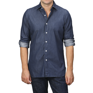 A man dressed in a stylish, fitted Medium Blue Cotton Denim Casual Shirt from Finamore, with rolled-up sleeves, paired flawlessly with dark jeans.