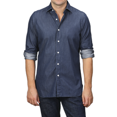 A man dressed in a stylish, fitted Medium Blue Cotton Denim Casual Shirt from Finamore, with rolled-up sleeves, paired flawlessly with dark jeans.