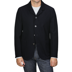 A person is casually dressed in a navy blue boiled wool blazer from Finamore, featuring patch pockets, over a crisp white shirt and jeans.