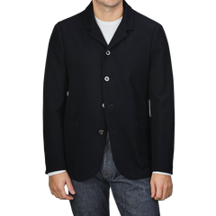 A person is casually dressed in a navy blue boiled wool blazer from Finamore, featuring patch pockets, over a crisp white shirt and jeans.