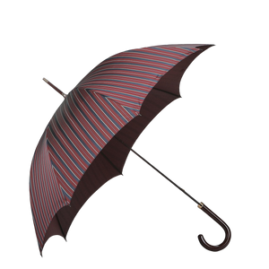 The Fox Umbrellas Red Blue Striped Maple Handle Umbrella, showcasing red, blue, and green diagonal patterns, features a crook handle made of elegantly curved wood. It stands open against a light gray background.