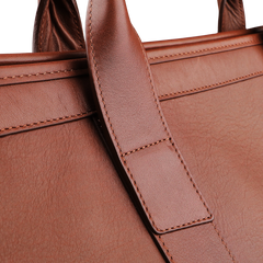 Close-up of the Frank Clegg Chestnut Tumbled Leather Signature Travel Duffle, highlighting its textured surface and the hand-crafted quality seen in the handle's stitching.