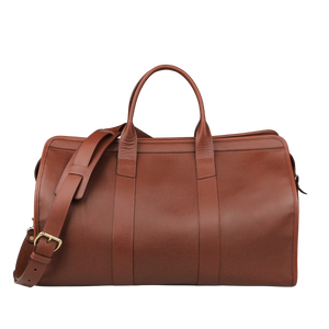 The Frank Clegg Chestnut Tumbled Leather Signature Travel Duffle boasts double handles and an adjustable strap, perfect for those seeking handcrafted quality against a neutral backdrop.