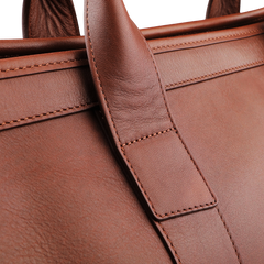 A close-up of the Chestnut Tumbled Leather Small Travel Duffle by Frank Clegg showcases intricate stitching and texture on the handle and body.