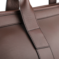 Zoom in on the handle of the Frank Clegg Chocolate Harness Belting Leather Signature Duffle, revealing its brown leather with visible stitching and a smooth texture that highlights its handcrafted quality.